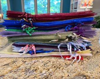May include: A stack of rectangular organza drawstring gift bags in a variety of colors including red, blue, green, purple, yellow, and white. Each sheer fabric pouch features a matching satin ribbon tie closure at the top for securing contents.