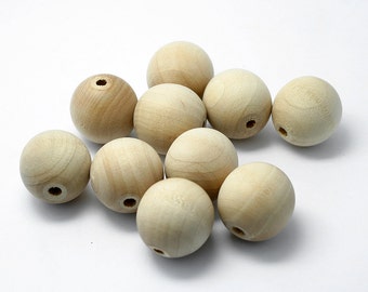 May include: A collection of eleven unfinished wooden round beads. Each bead is a light beige color with a smooth surface and a drilled hole. The beads are scattered on a white background. The beads are suitable for crafting.