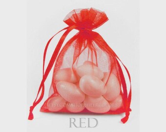 May include: A small, translucent red organza drawstring bag filled with several smooth, pale pink oval-shaped candies. The bag features a gathered top with matching red ribbon ties. The text "ETSY.COM/SHOP/SHEERCOLORS" and "RED" are visible.