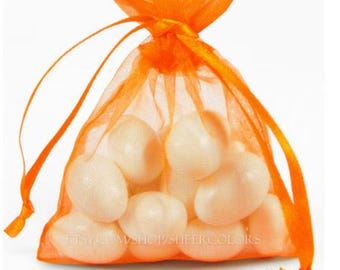 May include: A bright orange sheer organza drawstring pouch filled with several smooth, opaque, off-white oval-shaped objects. The bag is gathered at the top with matching orange ribbon ties, creating a translucent, lightweight appearance.