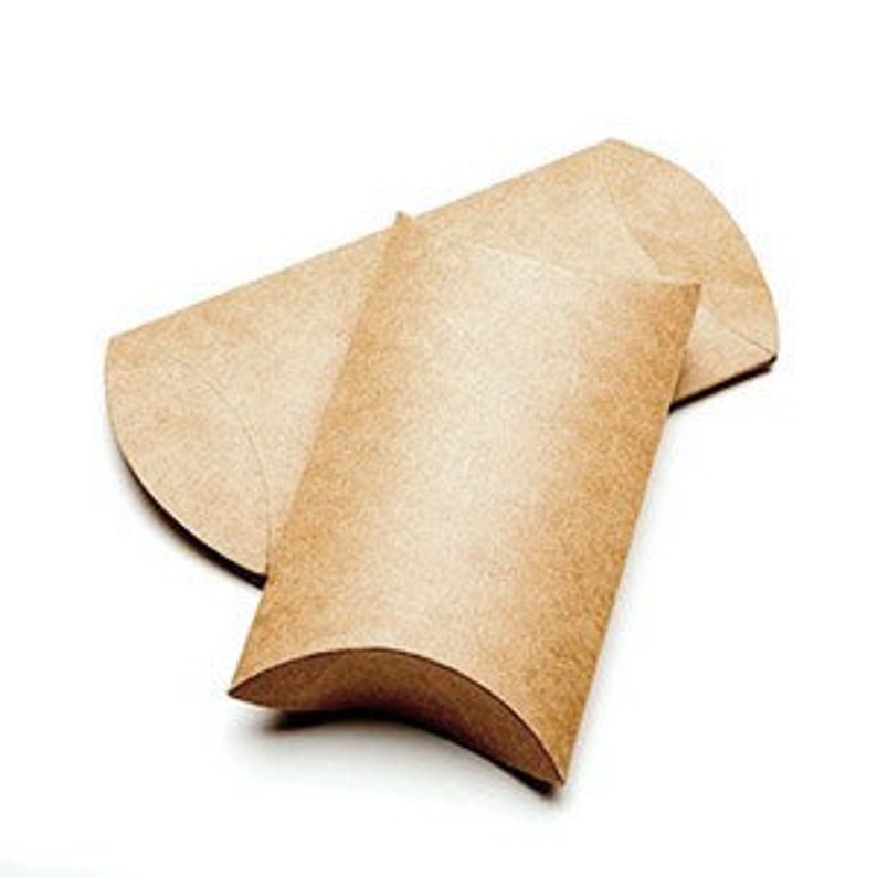 Puede incluir: Dos cajas de regalo marrones en forma de almohada se muestran sobre un fondo blanco. Las cajas est&aacute;n hechas de un material de papel reciclado texturizado. Una caja est&aacute; abierta, revelando su interior, mientras que la otra est&aacute; cerrada, mostrando su forma curva.