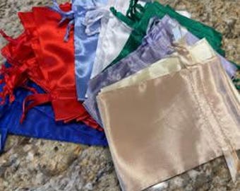 May include: A collection of rectangular satin drawstring pouches in various colors including red, blue, white, green, purple, and champagne. Each pouch features a matching satin ribbon closure at the top, creating a gathered opening for storage.