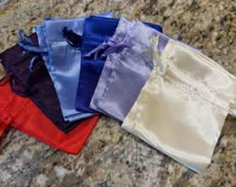 May include: A collection of five small drawstring pouches made of a smooth, shiny fabric. The pouches are arranged in a fan shape and feature a variety of colors including red, dark purple, light blue, royal blue, lavender, and cream.