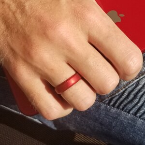 May include: A red silicone ring on a person's finger. The ring is smooth and has a matte finish.