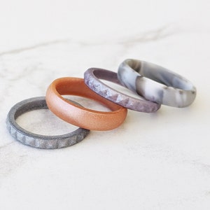 May include: Four silicone rings in different colors and patterns. The rings are stacked on top of each other. The rings are a light gray with a textured pattern, a light purple with a marbled pattern, a light gray with a marbled pattern, and a copper color.