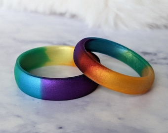 Puede incluir: Dos anillos de silicona coloridos, uno con un degradado de verde, amarillo y morado, y el otro con un degradado de naranja, amarillo y verde.