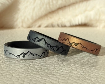 May include: Three silicone rings with a mountain range design. The rings are in black, gray, and copper.