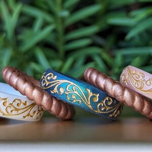 Peut inclure: Cinq bagues en silicone empilables avec un motif floral doré. Les bagues sont dans des tons de blanc, cuivre, turquoise et rose.