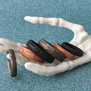 May include: Five silicone rings with a skeleton design. The rings are in different colors, including black, gray, brown, and copper.
