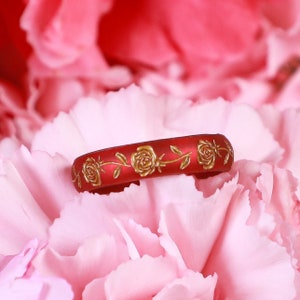 May include: A red silicone ring with a gold floral design. The ring is decorated with roses and leaves.