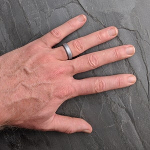 Op de afbeelding: Een close-up van een hand met een zilveren siliconen ring. De ring is simpel en modern, met een gladde, matte afwerking.