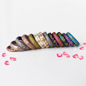 May include: A set of 12 silicone rings with a floral design in gold. The rings are in various colors, including copper, gray, pink, green, white, blue, purple, teal, and black.