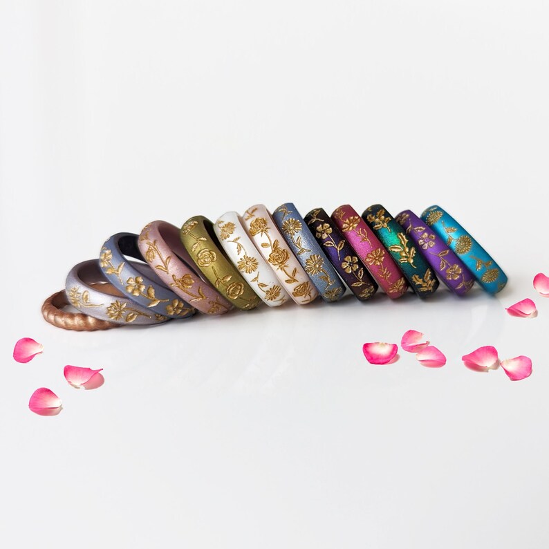 May include: A set of 12 silicone rings with a floral design in gold. The rings are in various colors, including copper, gray, pink, green, white, blue, purple, teal, and black.