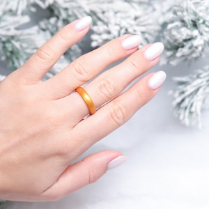 Puede incluir: Un anillo de silicona dorado en una mano con esmalte de uñas blanco.