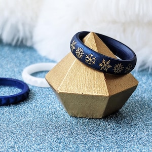 May include: A dark blue silicone ring with gold snowflake designs on a gold pyramid-shaped ring holder.