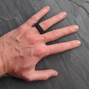 Op de afbeelding: Een close-up van een hand met een zwarte siliconen ring.