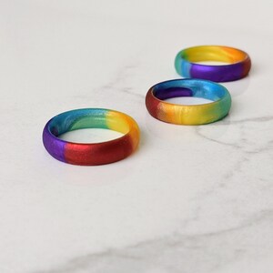 Puede incluir: Tres anillos de silicona arco&iacute;ris, cada uno con una combinaci&oacute;n de colores diferente. Los anillos est&aacute;n apilados uno encima del otro, siendo el anillo superior el m&aacute;s vibrante.