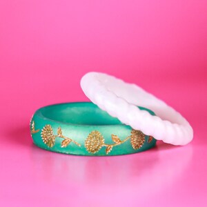 May include: Two silicone rings, one white and one green with gold floral designs.