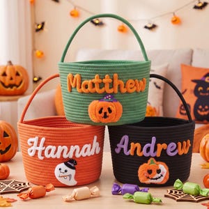 May include: Three round rope baskets for Halloween. The top green basket features the name Matthew and a pumpkin. The bottom left orange basket displays the name Hannah and a ghost. The bottom right black basket shows the name Andrew and a pumpkin.