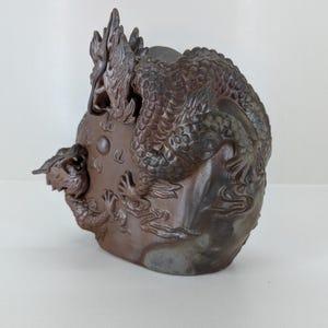 May include: A brown ceramic sculpture of a dragon coiled around a rock. The dragon has detailed scales and a long, serpentine body. The sculpture is a decorative item.