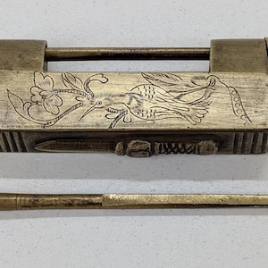 May include: Vintage brass lock featuring an engraved bird and floral design, accompanied by a key. The lock is rectangular with a sliding bar. The key is a long, thin rod with a hook at one end.