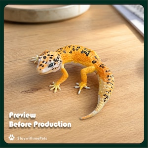 May include: A leopard gecko figurine with bright orange and yellow skin covered in dark brown spots. The lizard has a textured body, four legs with visible toes, and a thick, curved tail. The text "Preview Before Production" and "StaywithmePets" appear in the corner.