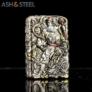 May include: A silver-toned metal lighter with intricate relief carvings. The design features a warrior figure with a long beard and a dragon. Gold and copper accents highlight the details. The text "ASH & STEEL" is at the top.