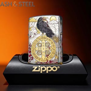 May include: A silver Zippo lighter with a detailed raven design, a cross, and the text "PAX" and "zippo&reg;". The raven is perched above a cross with the letters "C S S M D O P M B L". The lighter is displayed on a black stand.