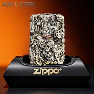 May include: A detailed, silver-toned Zippo lighter with an intricate relief design featuring a tiger and other figures. The lighter is displayed on a black stand with the Zippo logo in gold. The text "ASH & STEEL" is visible at the top.