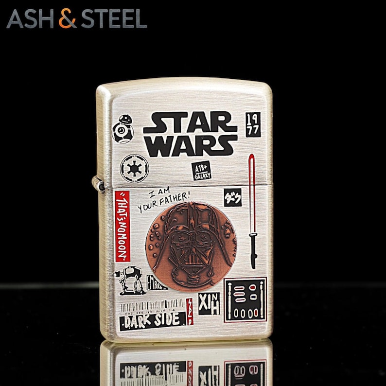 K&ouml;nnte beinhalten: Ein silberfarbenes Metallfeuerzeug mit Star Wars-Grafiken. Das Design umfasst das Star Wars-Logo, das Bild von Darth Vader und den Text "I AM YOUR FATHER!" und "DARK SIDE". Das Feuerzeug hat eine rechteckige Form und einen Klappdeckel.