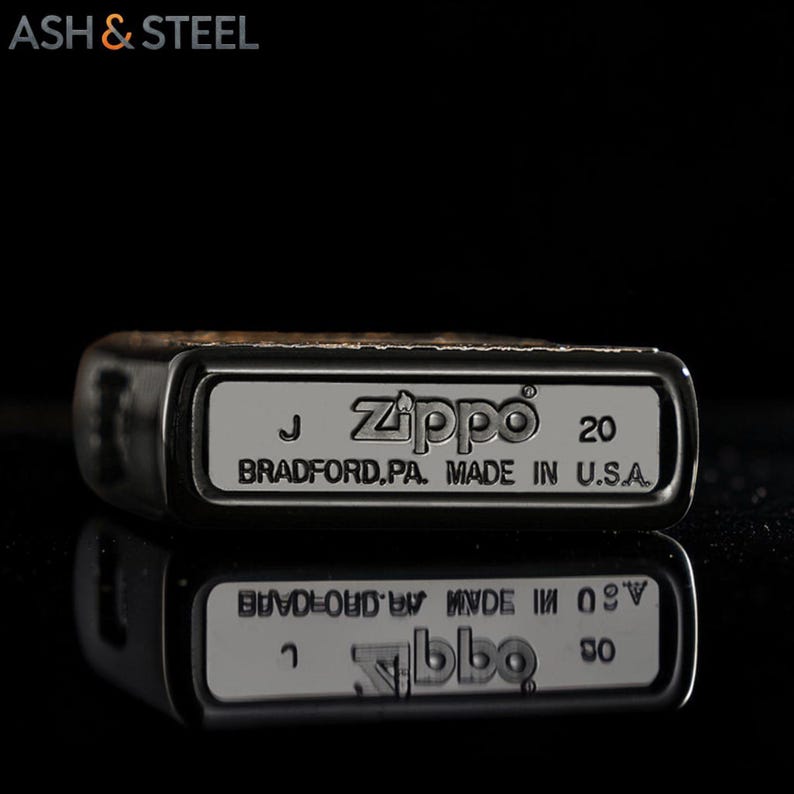May include: Close-up of a Zippo lighter with the text "Zippo" and "BRADFORD.PA. MADE IN U.S.A." The lighter is silver with a black border. The lighter's reflection is visible below it.