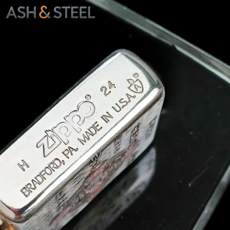 May include: Close-up of a silver Zippo lighter. The lighter is marked with the Zippo logo, the number 24, and "MADE IN U.S.A." The text "BRADFORD, PA" is also visible. The lighter is on a reflective surface.
