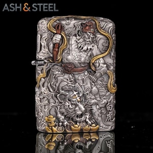 May include: A silver-colored lighter with intricate relief carvings. The design features a warrior figure, a tiger, and Chinese characters, with gold-colored accents. The brand name "ASH & STEEL" is at the top.