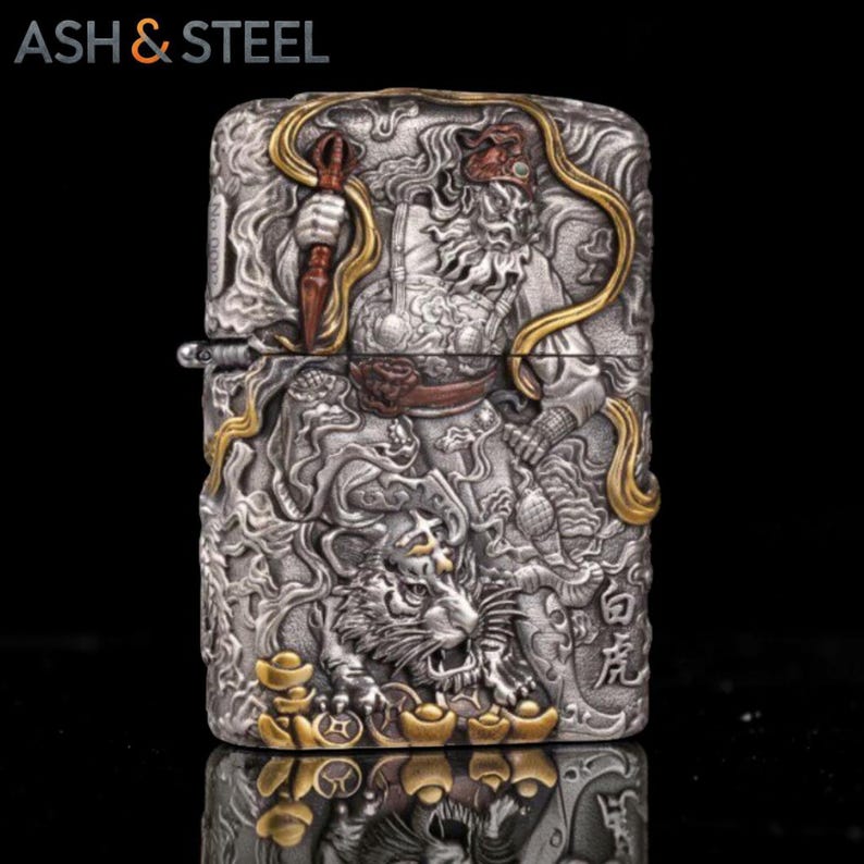 May include: A silver-colored lighter with intricate relief carvings. The design features a warrior figure, a tiger, and Chinese characters, with gold-colored accents. The brand name "ASH & STEEL" is at the top.
