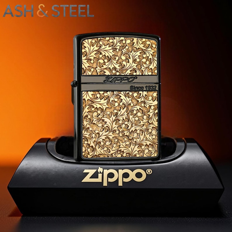 May include: Black Zippo lighter with a gold floral pattern. The lighter is displayed on a black stand with the Zippo logo. The text "Zippo Since 1932" is visible on the lighter.