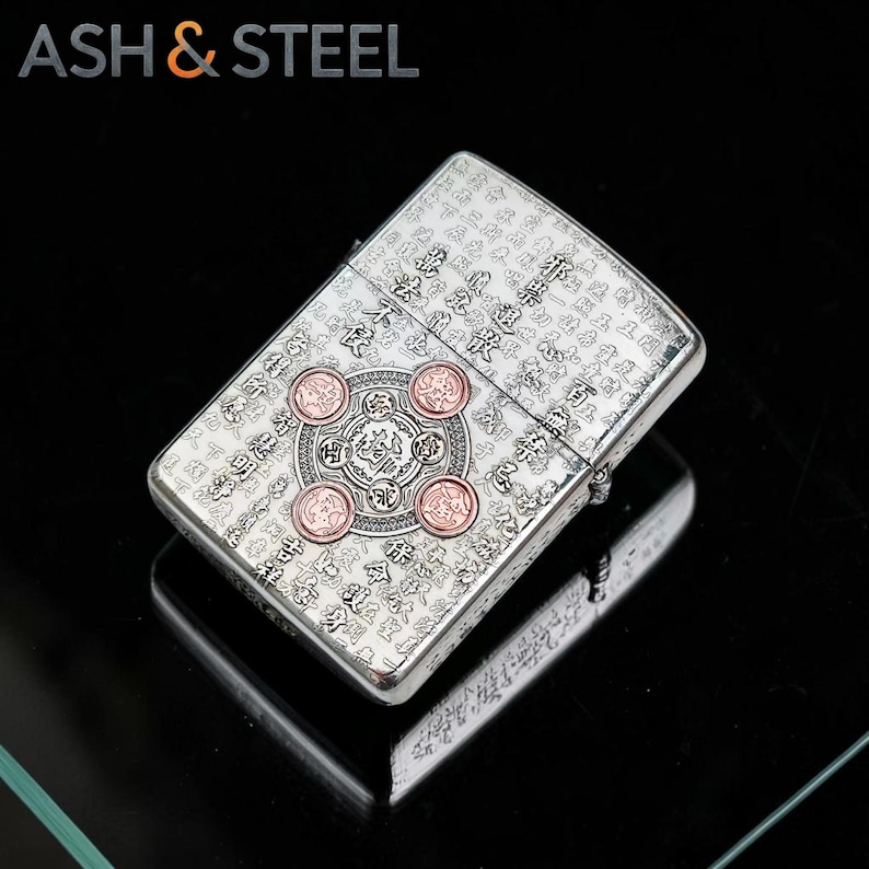 May include: Silver-colored lighter with intricate engraved patterns and four copper-colored circular accents. The lighter has a rectangular shape and features the text "ASH & STEEL" at the top. The design includes Asian-inspired calligraphy.