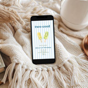 May include: A smartphone displaying a digital birthday invitation with a light blue and white vertical striped background. The text reads two cool, Oliver's 2nd Birthday, and includes illustrations of a yellow and a green popsicle on wooden sticks.