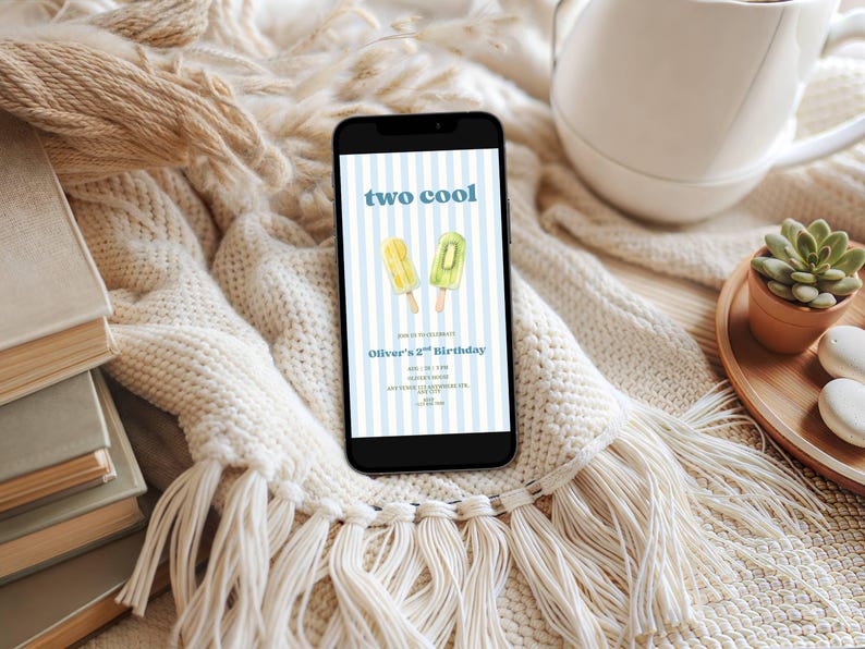 May include: A smartphone displaying a digital birthday invitation with a light blue and white vertical striped background. The text reads two cool, Oliver's 2nd Birthday, and includes illustrations of a yellow and a green popsicle on wooden sticks.