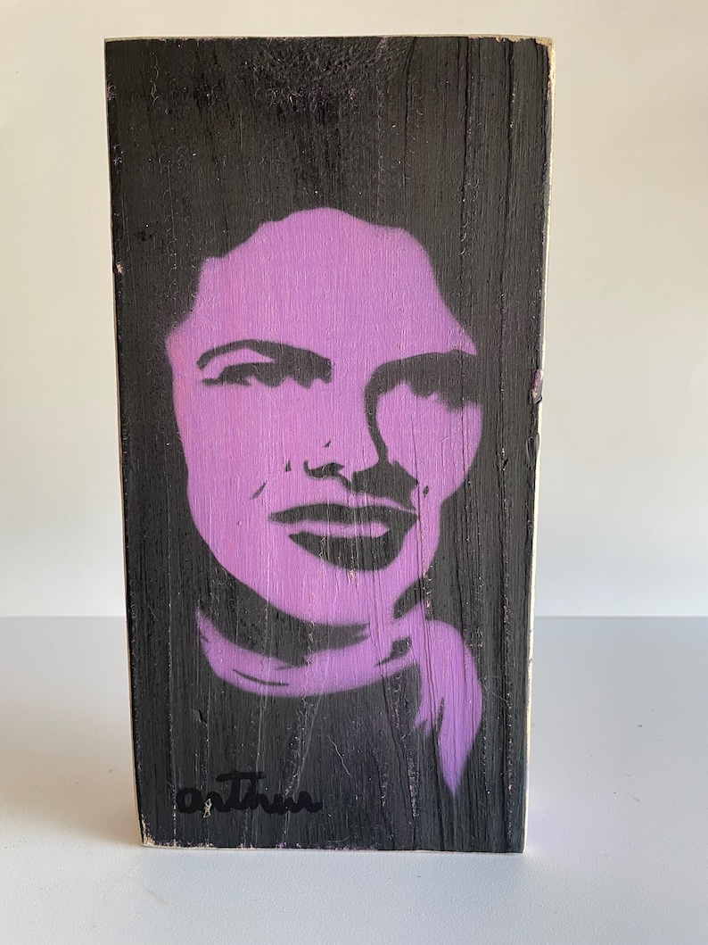 Peut inclure: Bloc de bois rectangulaire peint en noir, avec un portrait au pochoir violet d'un visage. Le bloc porte une signature, "o. Thru", &agrave; l'encre noire en bas. Le grain du bois est visible.