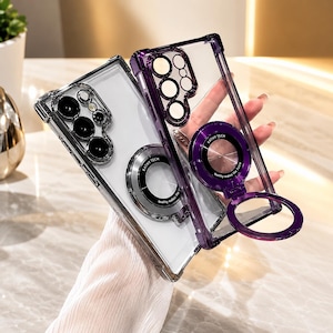 May include: Two clear phone cases with purple frames and integrated circular magnetic ring stands. The back of each case features a camera cutout and a circular metallic ring with the text KATHY TECH quality makes the future printed on it.