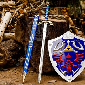 Puede incluir: Un conjunto de espada, vaina y escudo. La espada tiene una hoja plateada y un mango azul y plateado. La vaina es azul con detalles dorados. El escudo es azul con ribete plateado y detalles rojos y dorados.