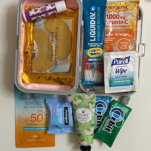 K&ouml;nnte beinhalten: Ein Reise-Set mit Sch&ouml;nheits- und Wellnessprodukten. Enth&auml;lt Lippenbalsam, Augenmasken, Sonnenschutzmittel LSF 50, Make-up-Entferner, Handcreme, Kaugummi, Elektrolyt-Getr&auml;nkemix, Vitamin-C-Beutel und H&auml;ndedesinfektionst&uuml;cher. Das Set befindet sich in einem rosa-grauen Etui.