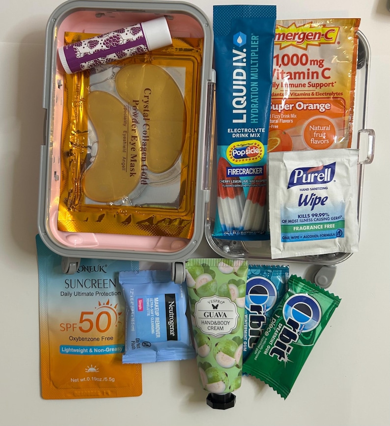 K&ouml;nnte beinhalten: Ein Reise-Set mit Sch&ouml;nheits- und Wellnessprodukten. Enth&auml;lt Lippenbalsam, Augenmasken, Sonnenschutzmittel LSF 50, Make-up-Entferner, Handcreme, Kaugummi, Elektrolyt-Getr&auml;nkemix, Vitamin-C-Beutel und H&auml;ndedesinfektionst&uuml;cher. Das Set befindet sich in einem rosa-grauen Etui.