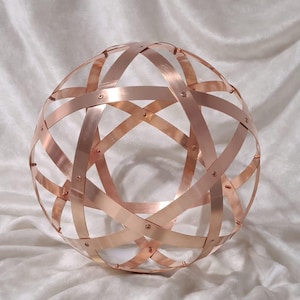 Può includere: Scultura sferica color rame con fasce metalliche intersecanti, che creano un design traforato. Le fasce sono rivettate in vari punti, formando un motivo geometrico. Oggetto decorativo.