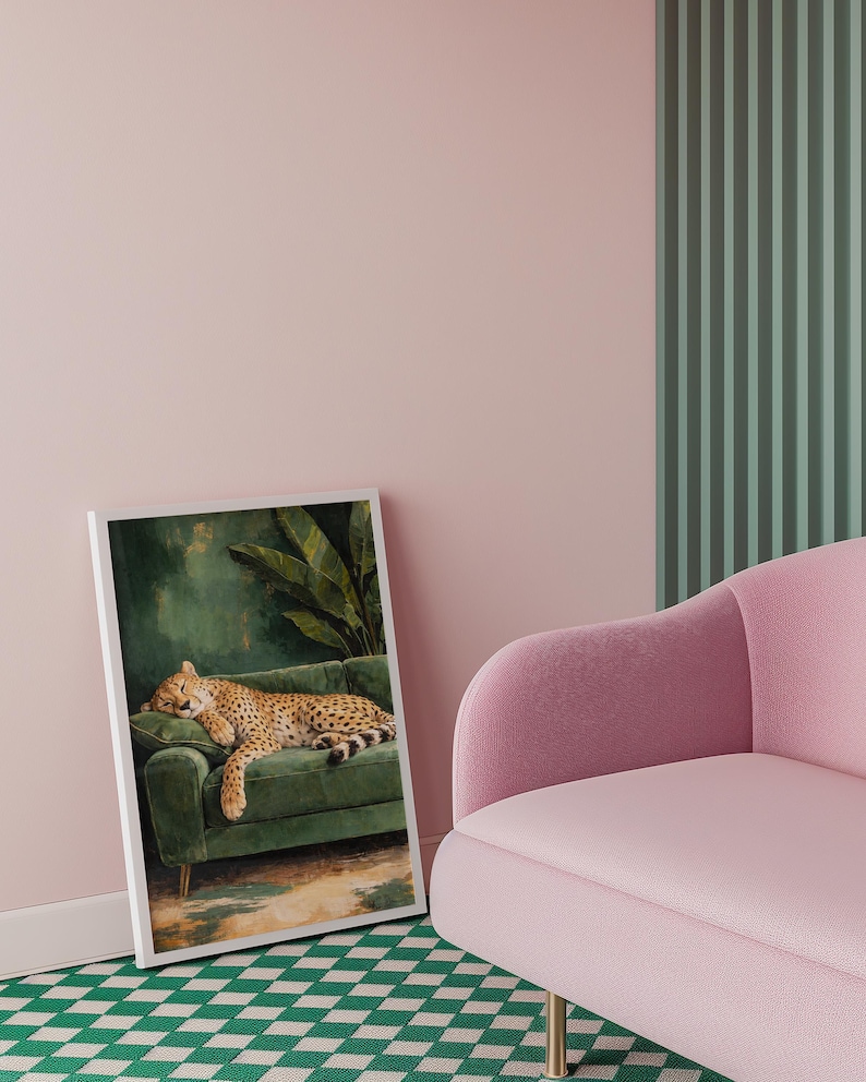 May include: A framed art print depicts a cheetah resting on a green velvet sofa. The cheetah has a spotted coat and is lying down. The background of the print is a dark green with a large leaf. The print is leaning against a pink wall.