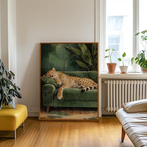May include: A framed art print depicts a cheetah resting on a green velvet sofa. The cheetah has a tan coat with black spots. The background features a dark green wall with large leaves. The frame is a warm brown color.