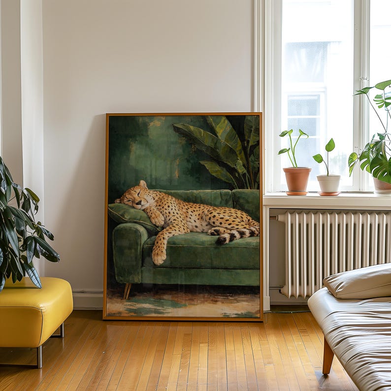 May include: A framed art print depicts a cheetah resting on a green velvet sofa. The cheetah has a tan coat with black spots. The background features a dark green wall with large leaves. The frame is a warm brown color.