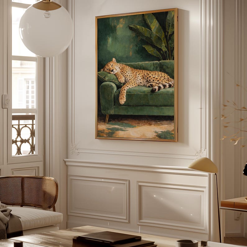 May include: A framed artwork depicts a sleeping leopard on a green velvet sofa. The painting features a gold frame and is set against a backdrop of lush green foliage. The artwork is displayed on a white wall.