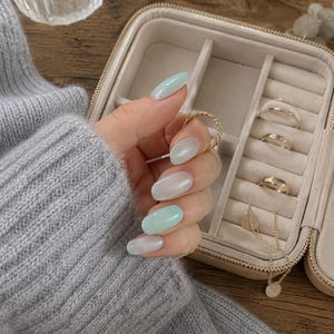 Puede incluir: Un joyero de color beige con múltiples compartimentos que contiene tres anillos dorados y un collar de cadena fina de oro con un colgante circular. El joyero cuenta con un forro interior de terciopelo suave y un cierre de cremallera.