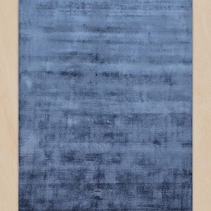 May include: A rectangular, blue area rug with a textured appearance. The rug has a gradient effect, transitioning from a lighter blue at the top to a darker blue at the bottom. The rug is placed on a light-colored wooden floor.